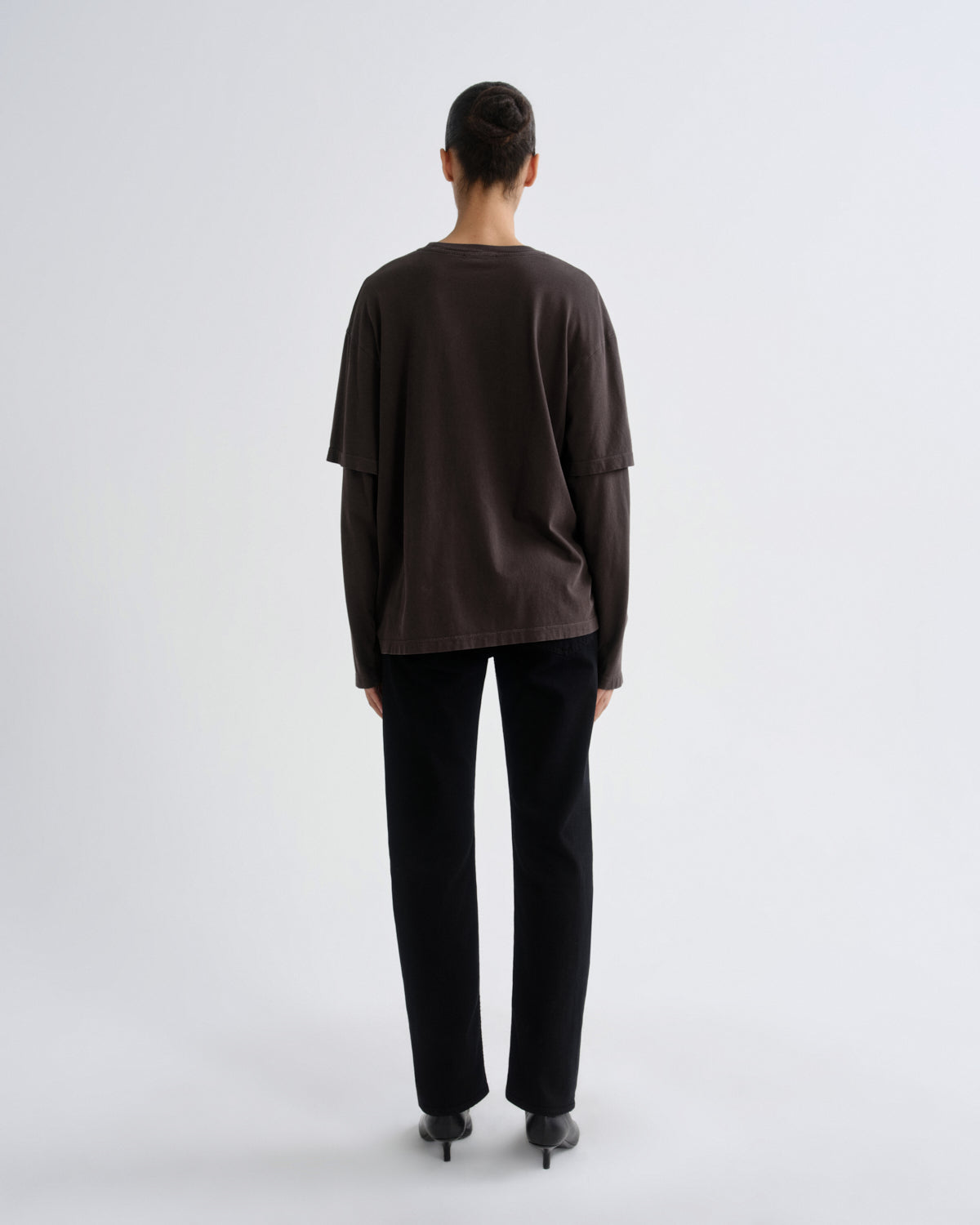 Person wearing a dark brown top and black pants on a white background