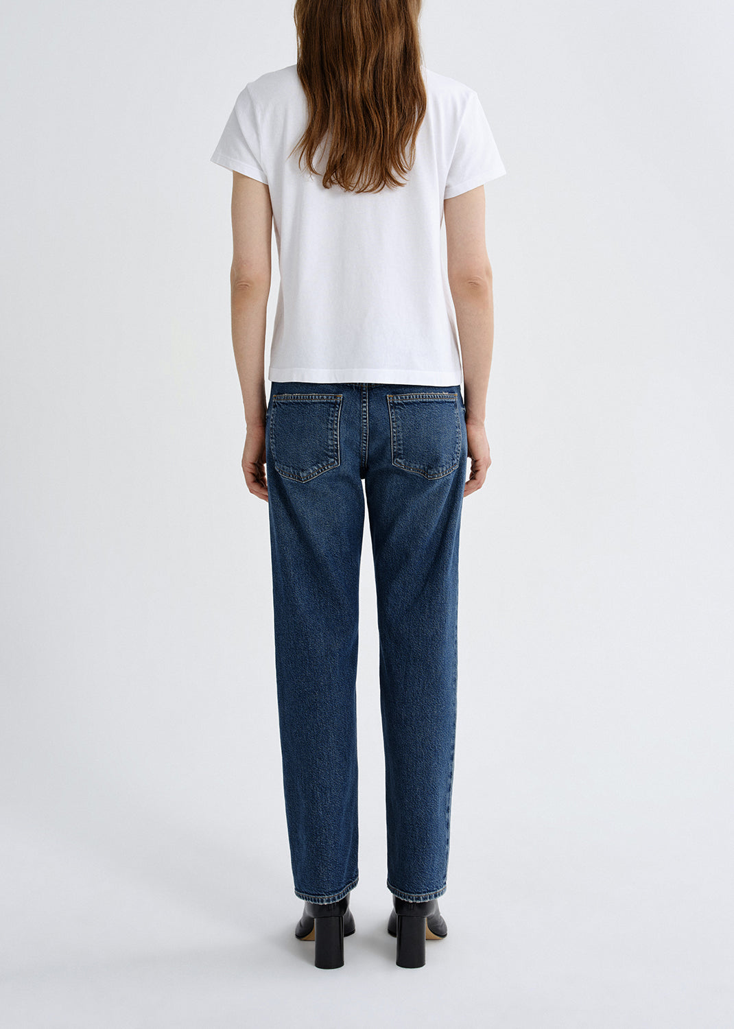 Person wearing blue jeans and a white t-shirt on a grey background