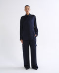 A model stands against a plain white studio background wearing a dark navy blue long-sleeve collared shirt and matching wide-leg cargo pants.
