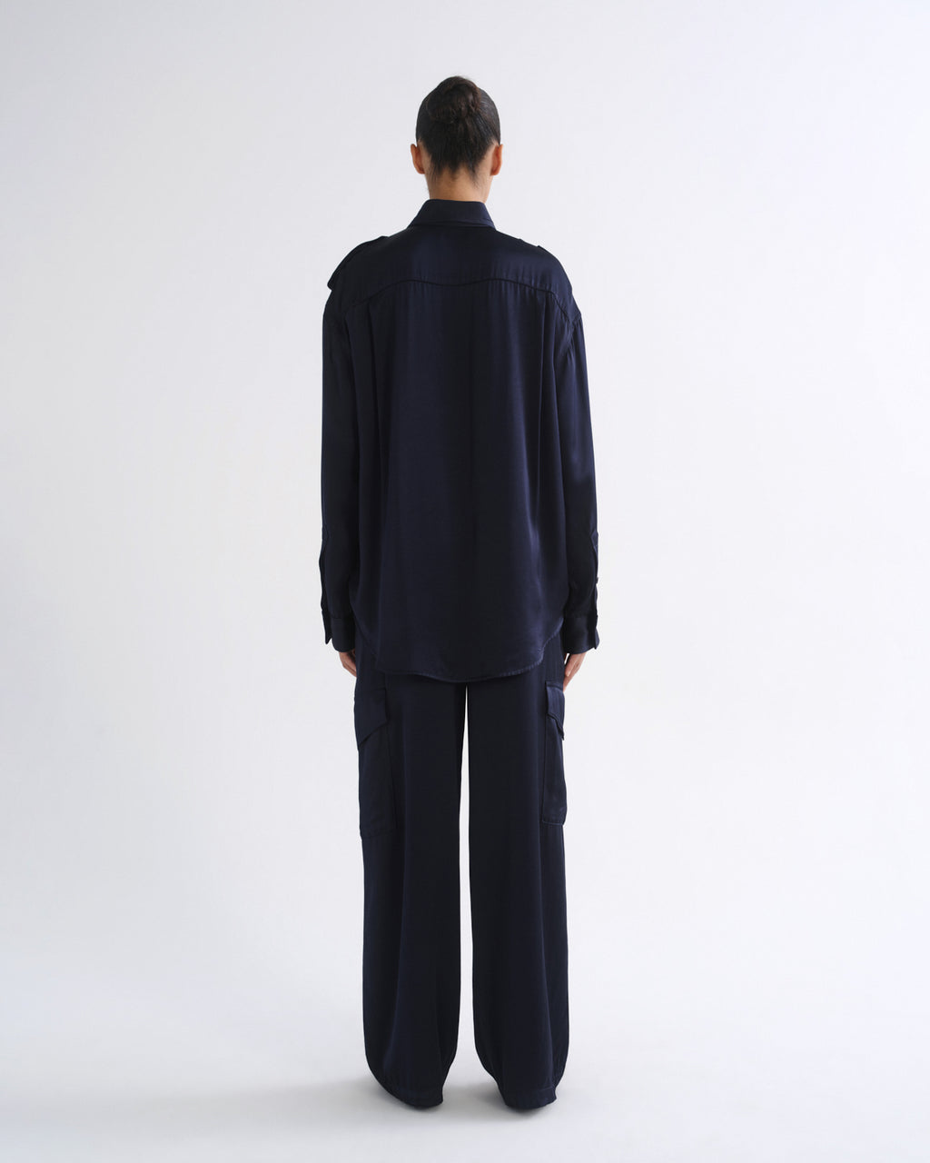 A model viewed from the back wearing a dark navy blue long-sleeve button-up shirt and matching wide-leg trousers against a plain white studio background.