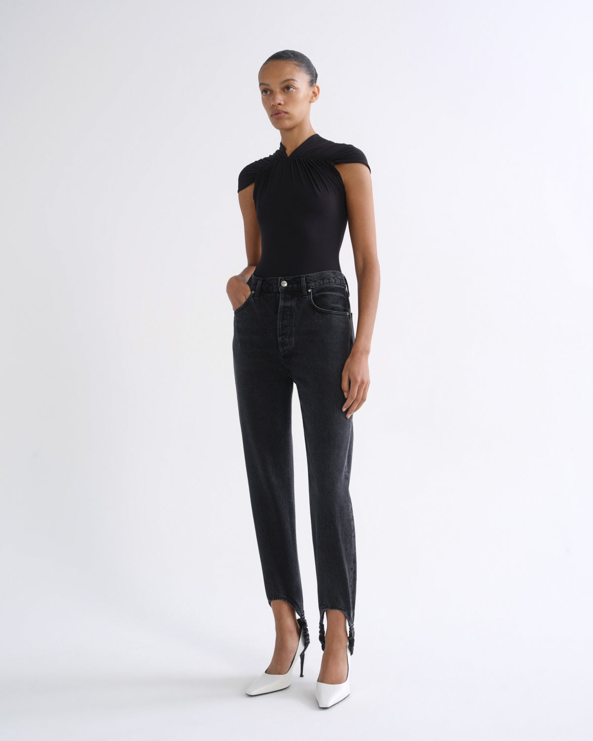 Woman wearing a black sleeveless top with black straight leg pants on a grey background.