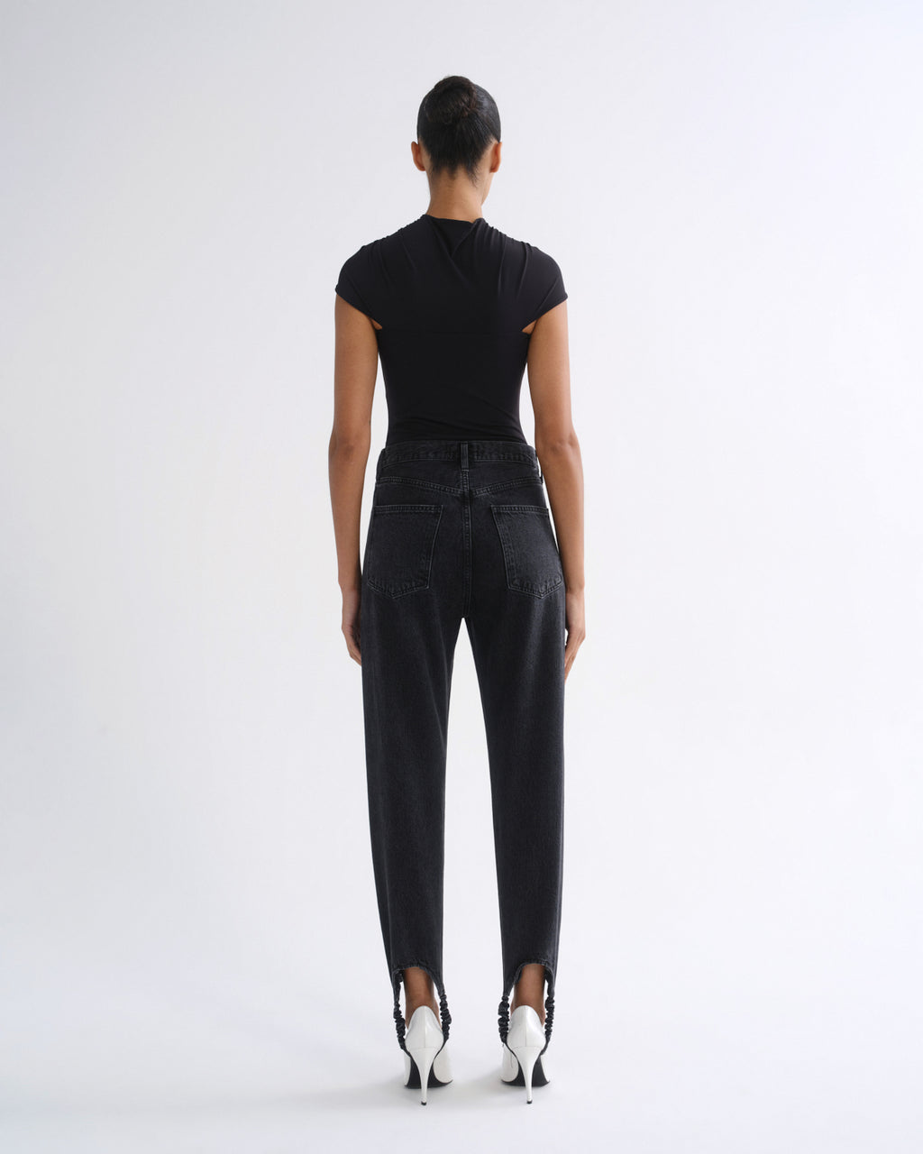 Woman wearing a black sleeveless top with black straight leg pants on a grey background.