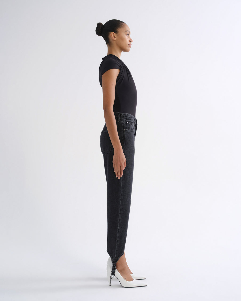 Woman wearing a black sleeveless top with black straight leg pants viewed from the side on a grey background.