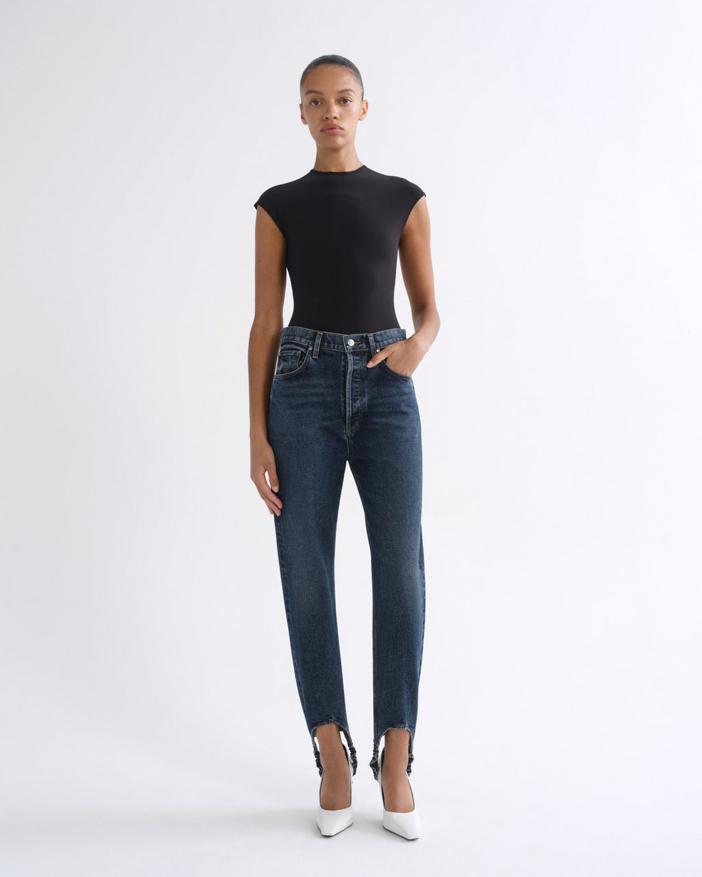 Woman wearing a black sleeveless top with dark indigo straight leg jeans on a grey background.