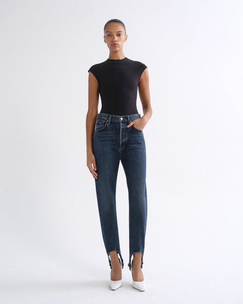 Woman wearing a black sleeveless top with dark indigo straight leg jeans on a grey background.