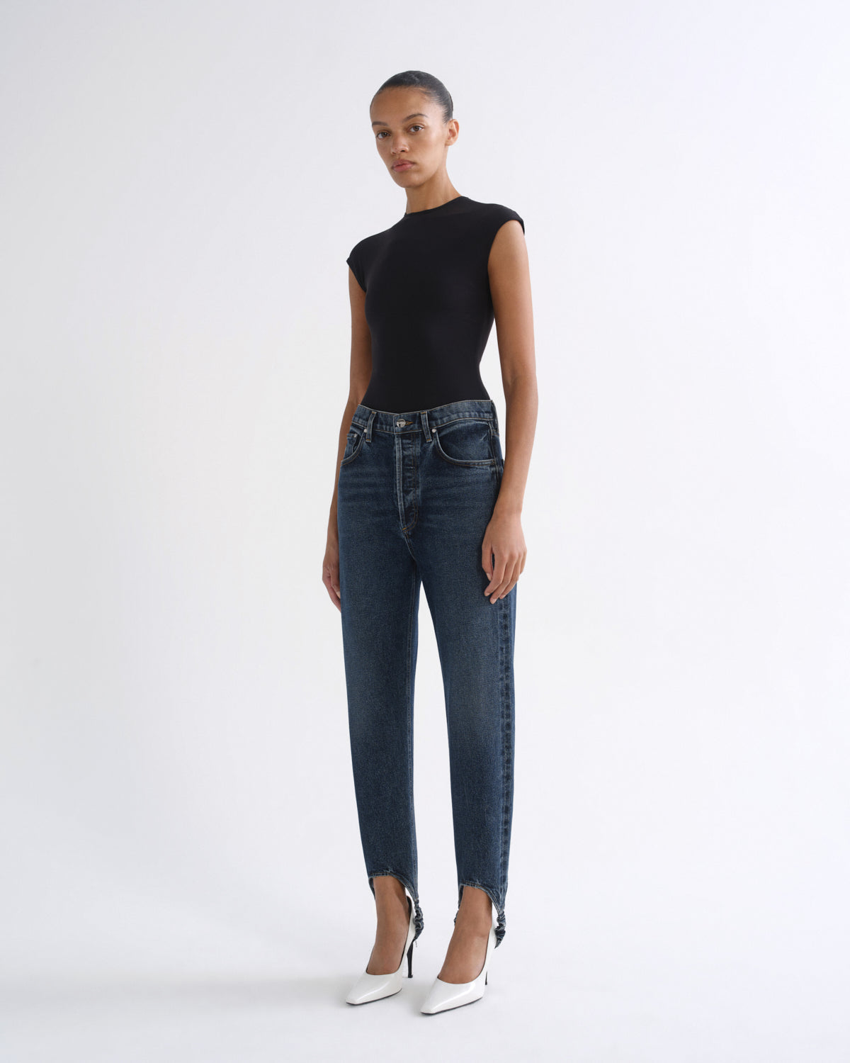 Woman wearing a black sleeveless top with dark indigo straight leg jeans on a grey background.