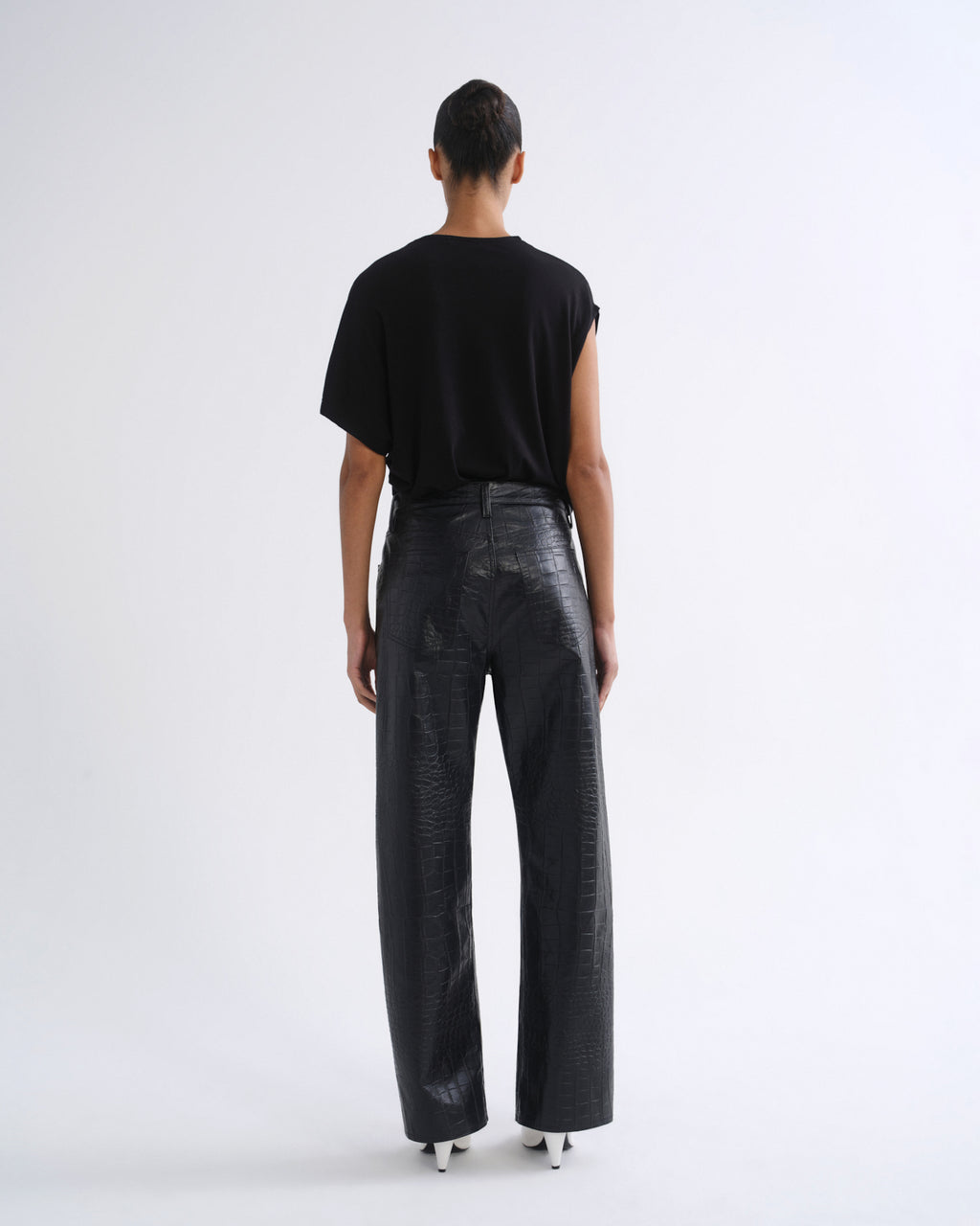 A model viewed from the back wearing a black short-sleeve t-shirt and black wide-leg textured pants, standing against a plain white studio background.
