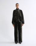 A model stands against a light gray studio background wearing a matching black velvet tracksuit with a high collar zip jacket and wide-leg cargo pants.