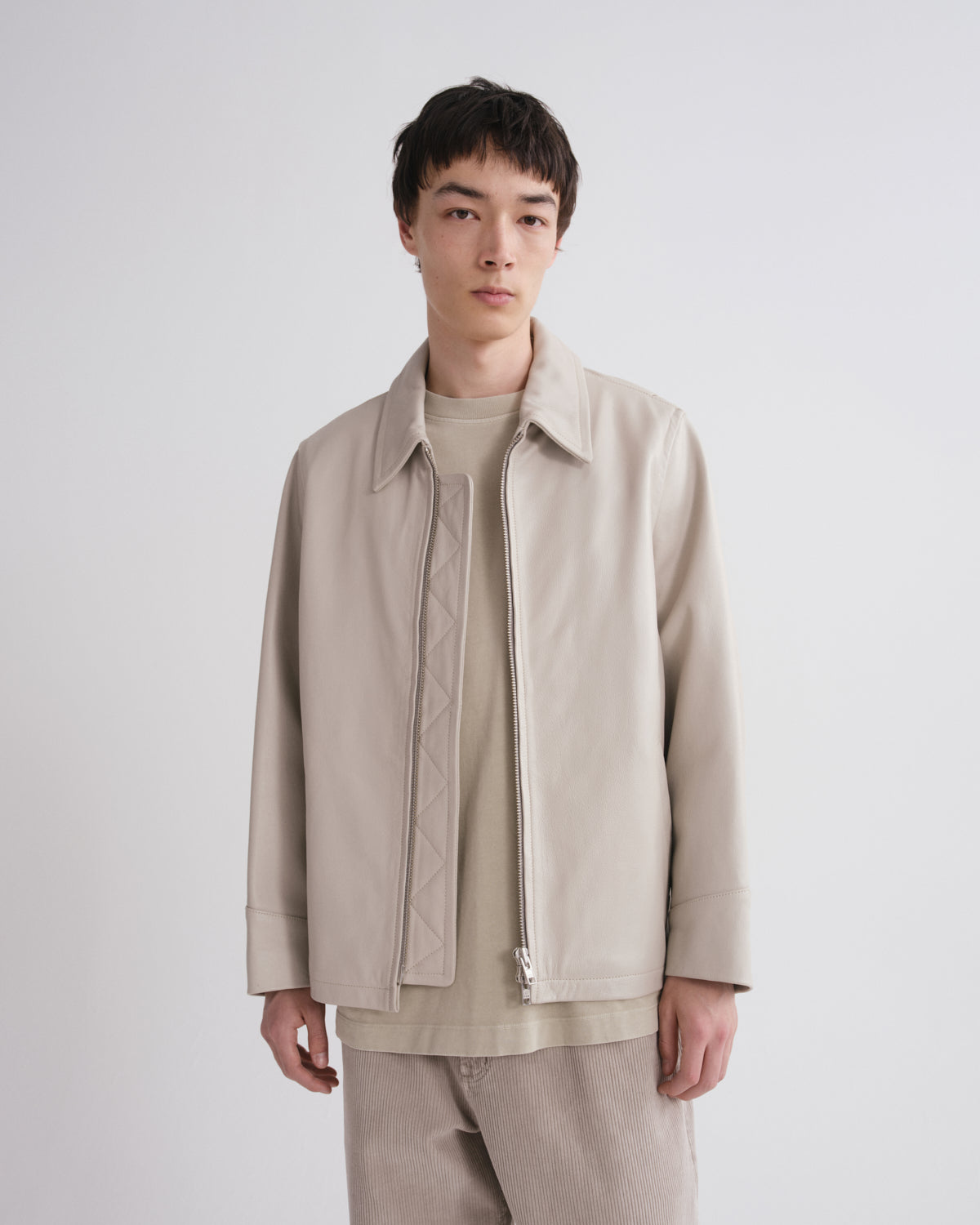 Man wearing a beige jacket and pants against a white background