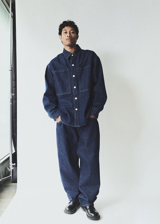Man wearing a blue denim outfit standing against a white wall.