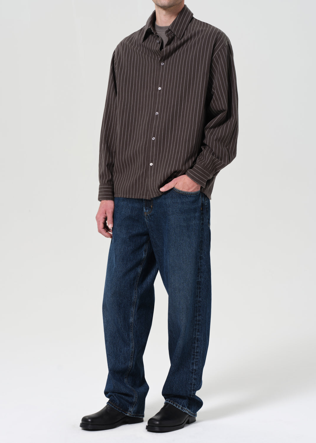 Person wearing a brown striped shirt and blue jeans on a white background