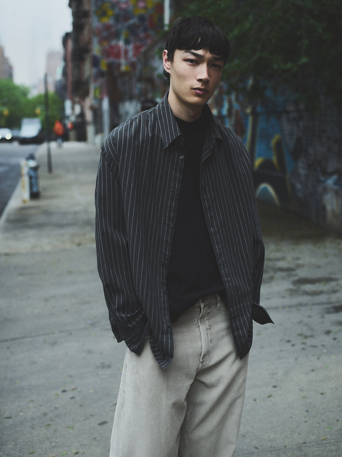 Man wearing a striped shirt and light pants on a street with graffiti in the background