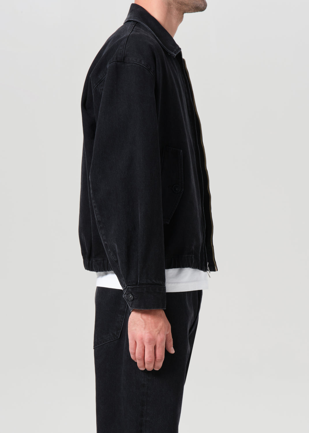 Person wearing a black jacket and dark pants on a light gray background