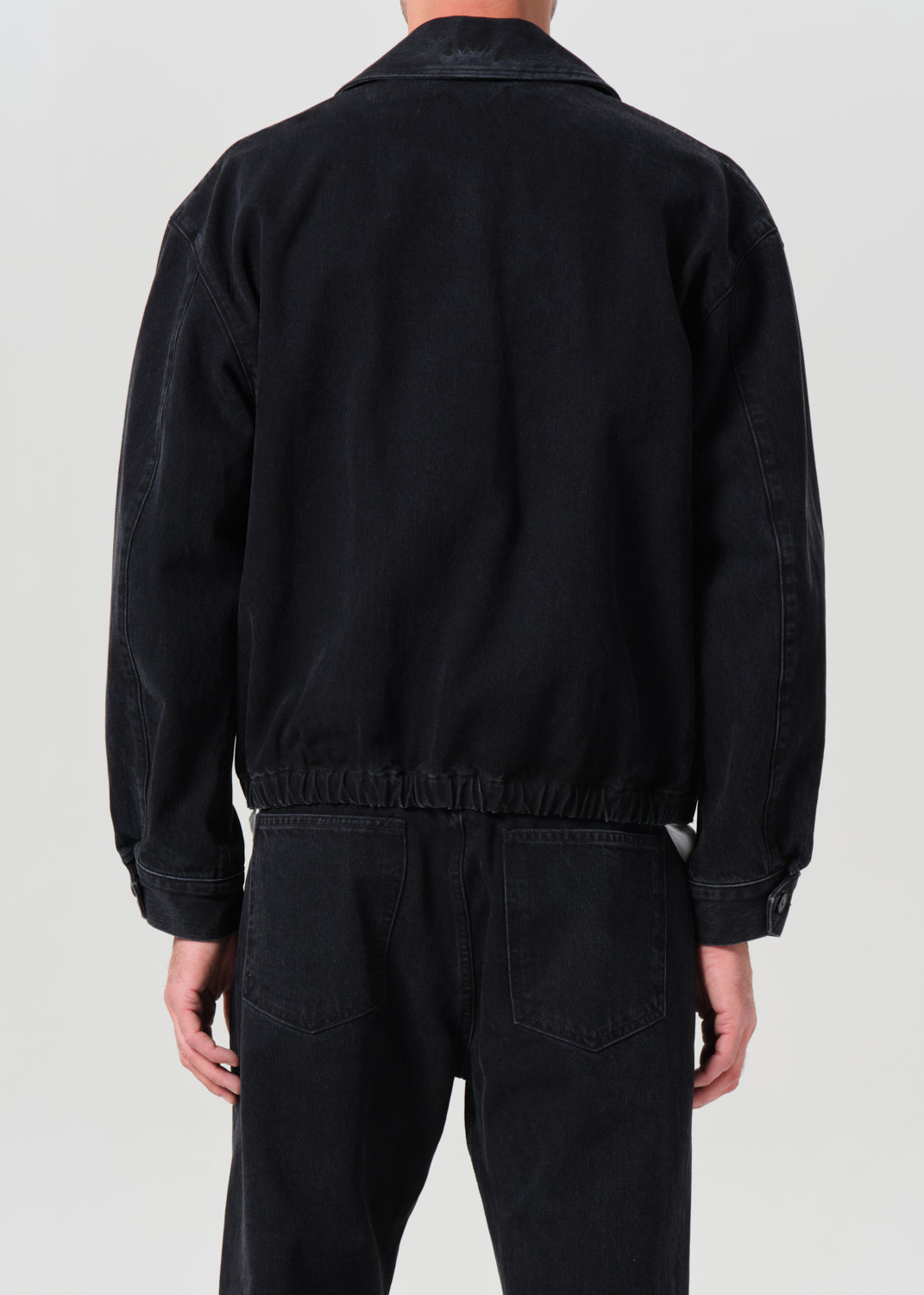 Person wearing a black jacket and pants on a light gray background