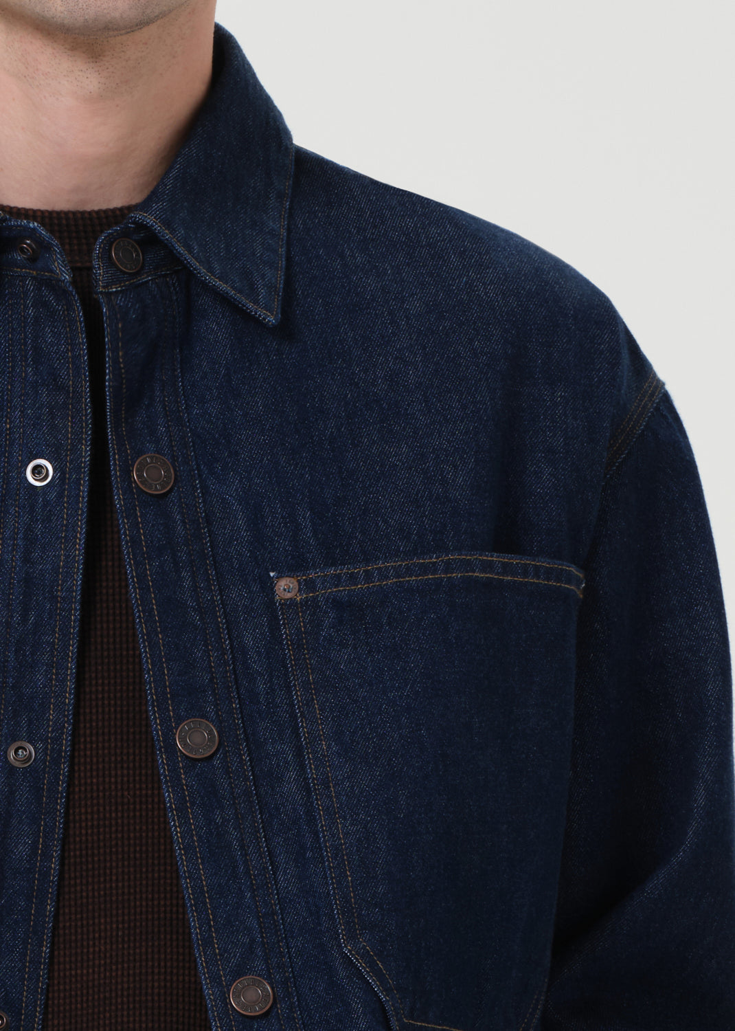 Close-up of a person wearing a dark blue denim jacket on a light gray background