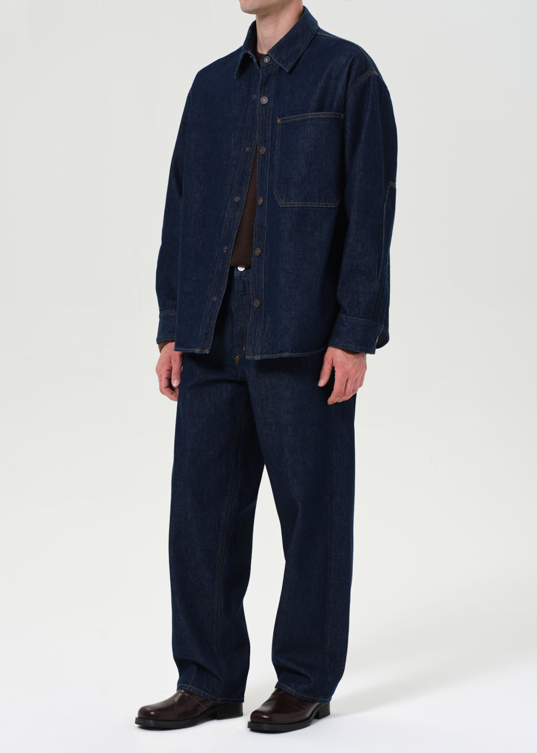 Person wearing a dark denim jacket and pants on a white background