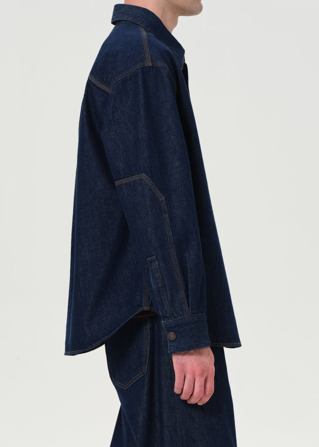 Person wearing a dark blue denim jacket and pants on a light gray background