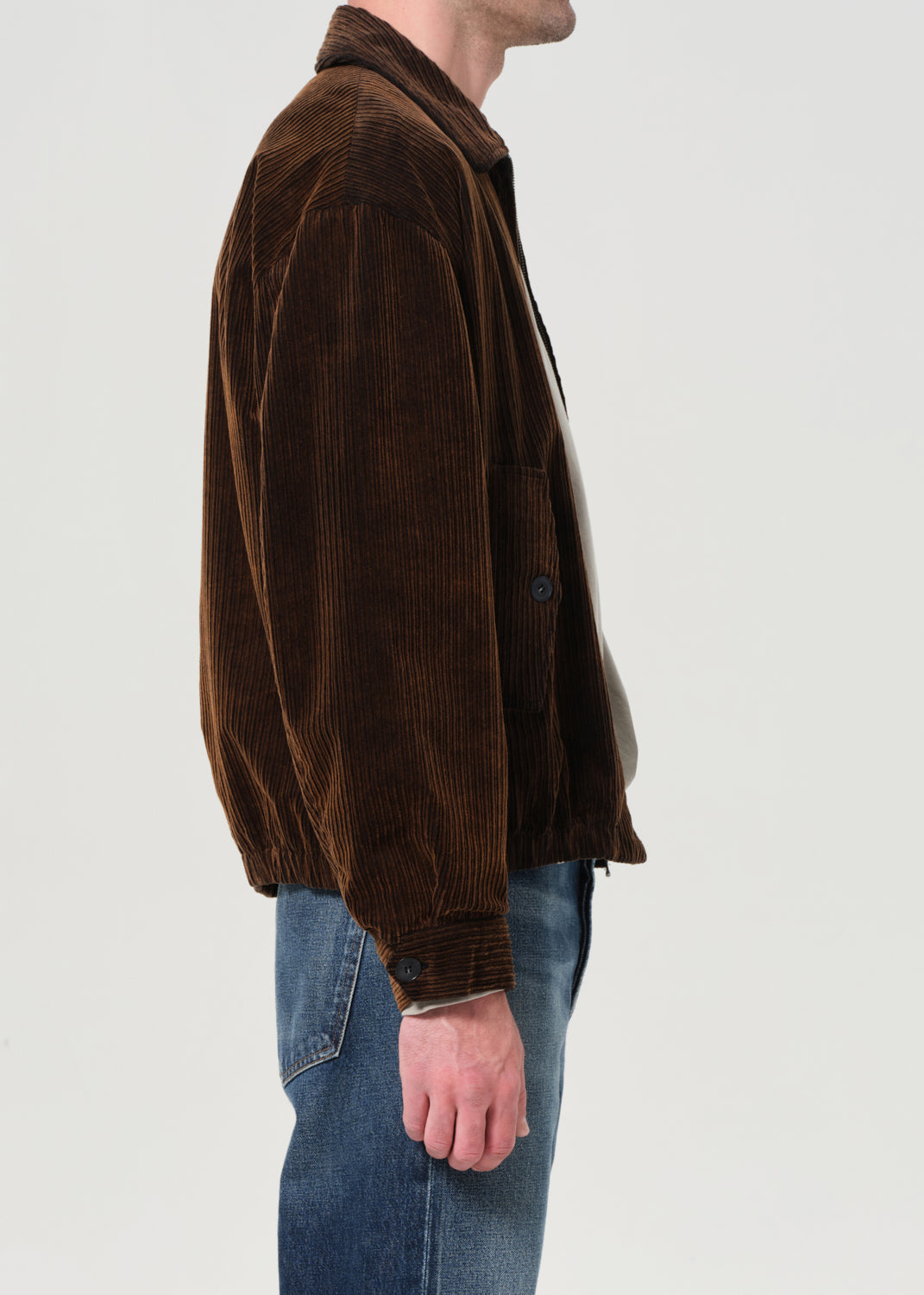 Person wearing a brown corduroy jacket and blue jeans on a white background