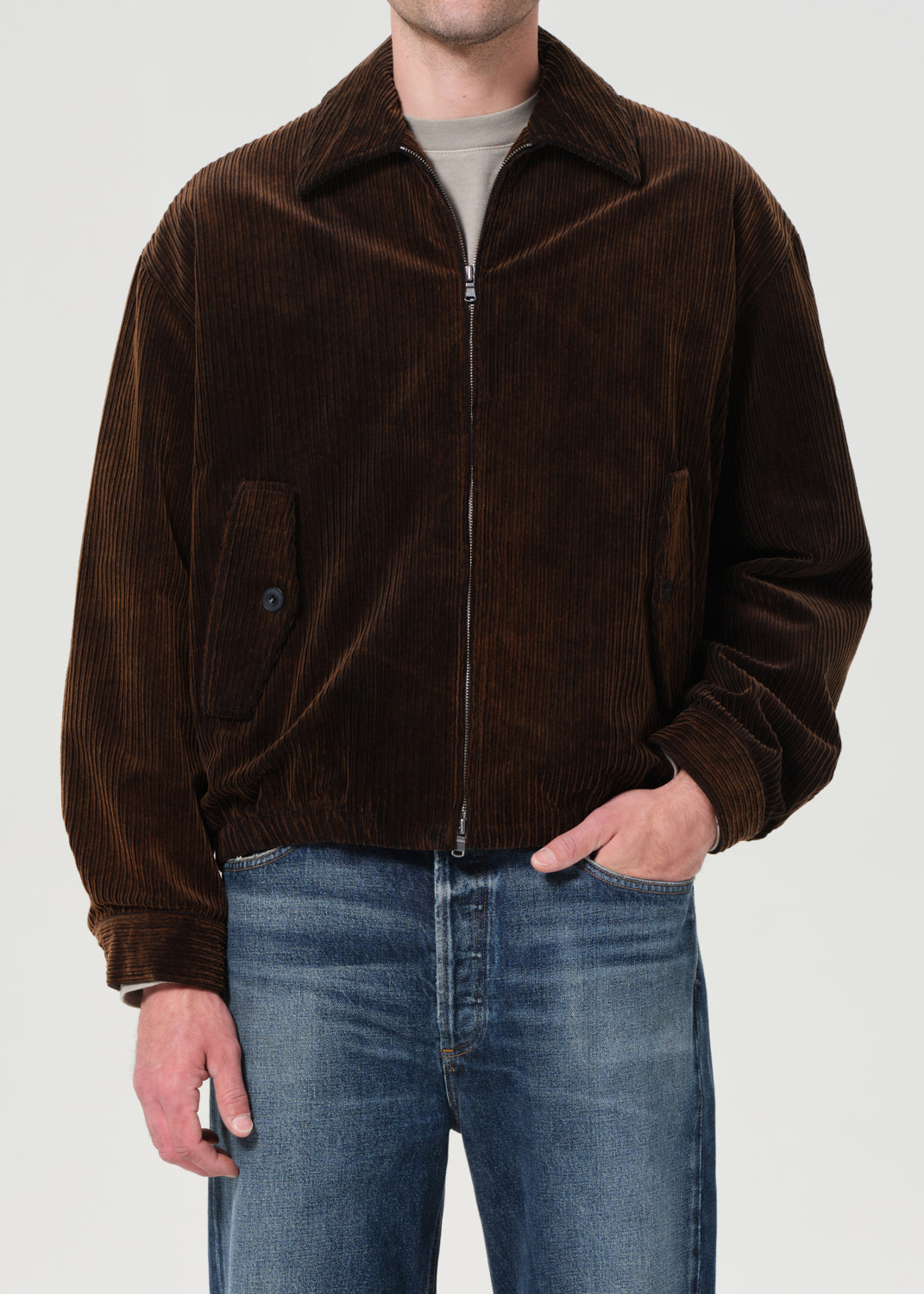 Man wearing a brown corduroy jacket and blue jeans on a plain background