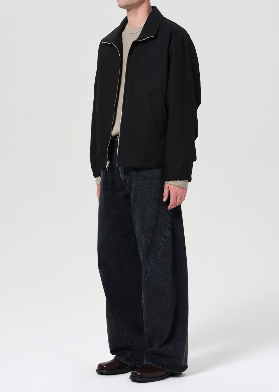 Person wearing a black jacket and dark pants on a white background