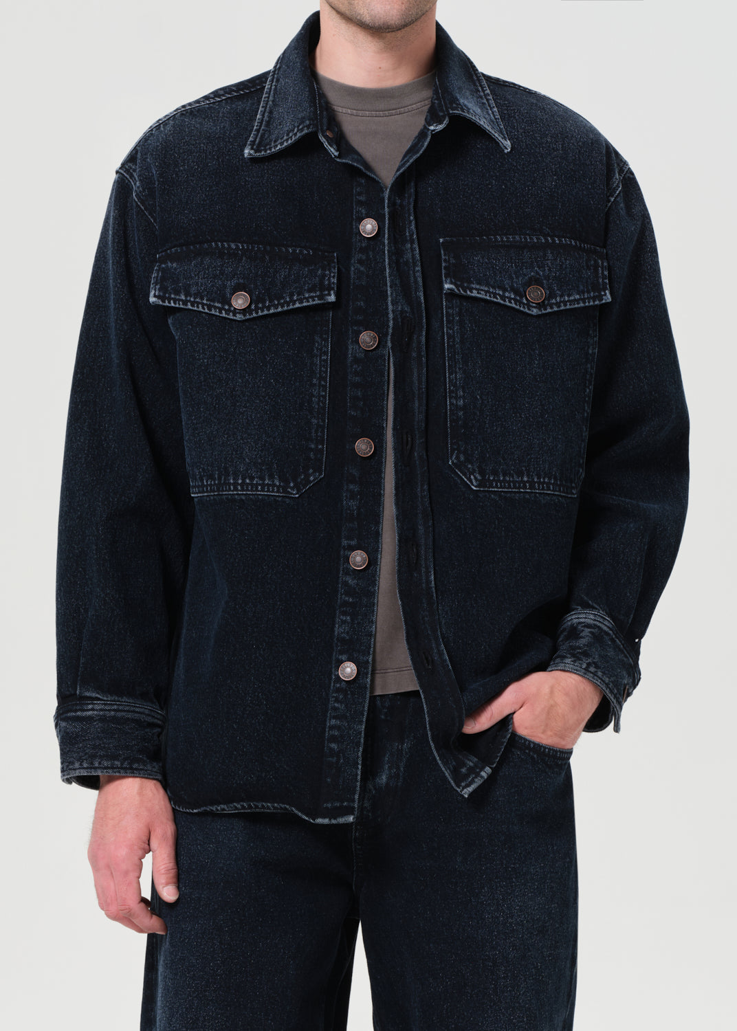 Person wearing a dark denim jacket on a plain background
