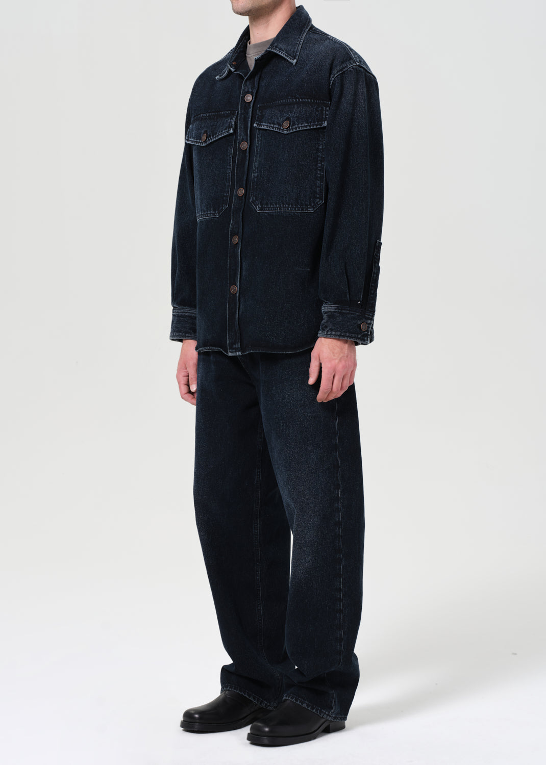 Person wearing a dark denim shirt and jeans on a white background