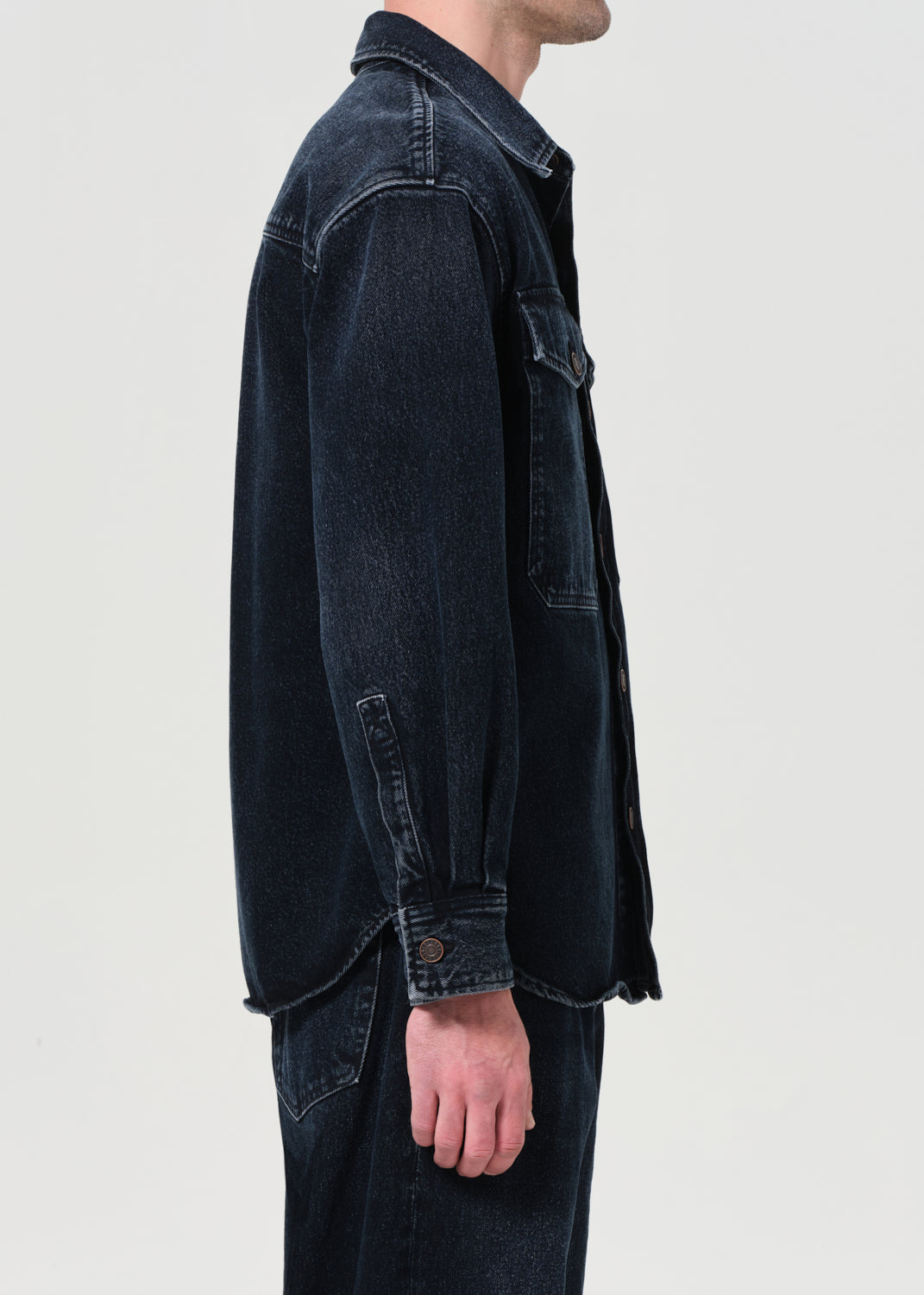 Person wearing a dark denim jacket on a plain background