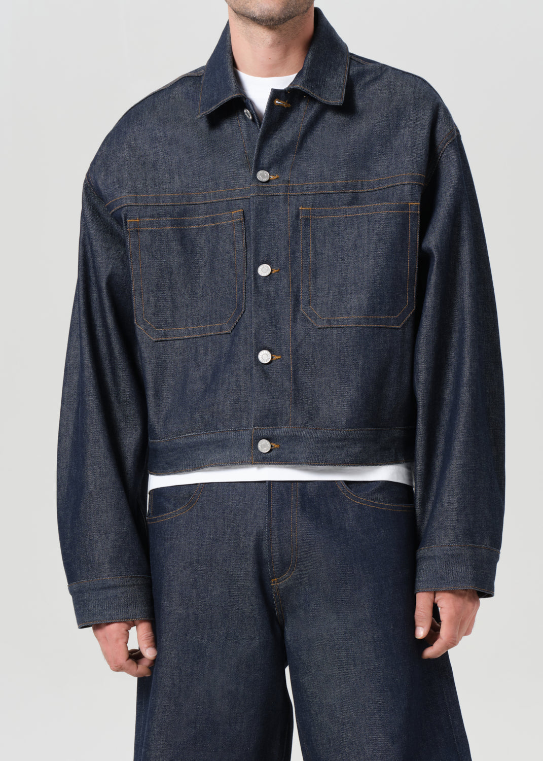 Person wearing a dark denim jacket and pants on a plain background