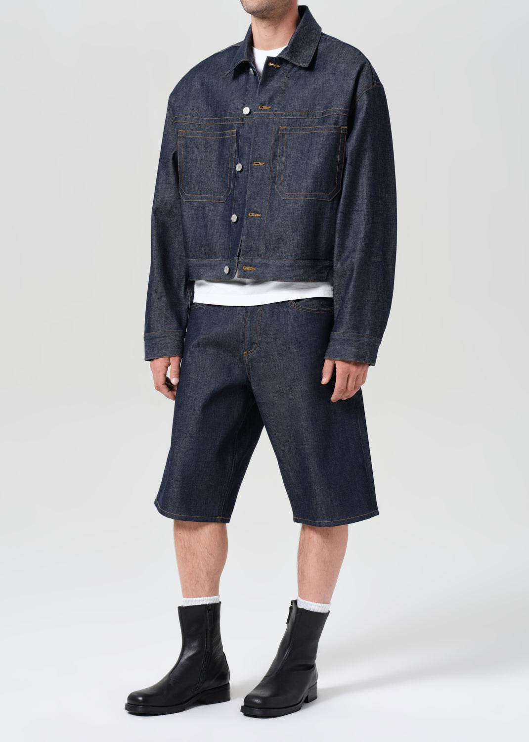 Person wearing a dark denim jacket and shorts with black boots on a white background