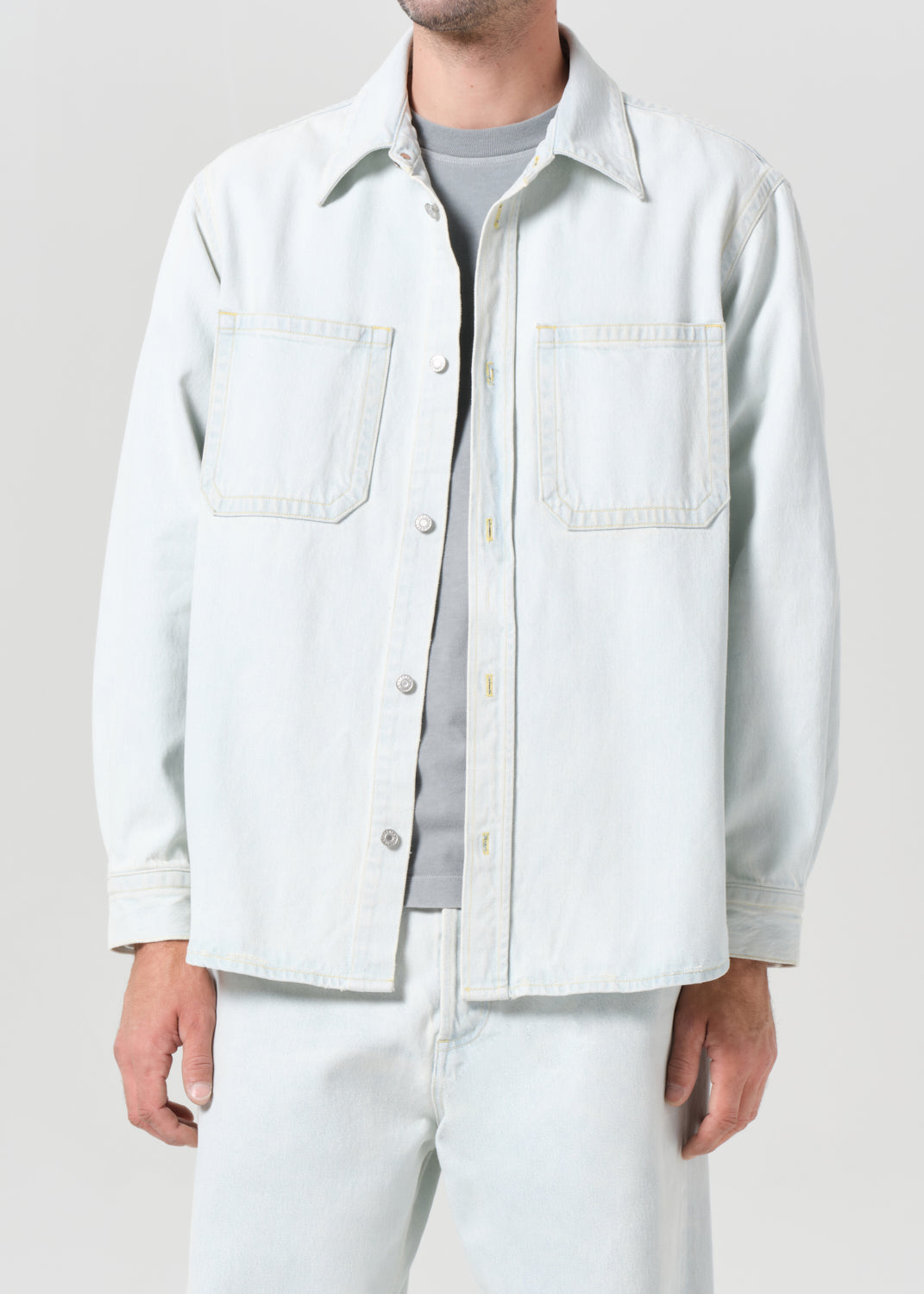 Person wearing a light-colored jacket over a shirt with white pants on a plain background