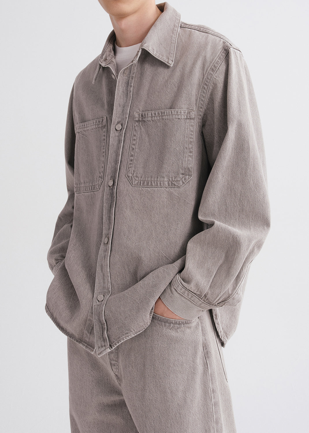 Person wearing a gray denim shirt and pants on a grey background