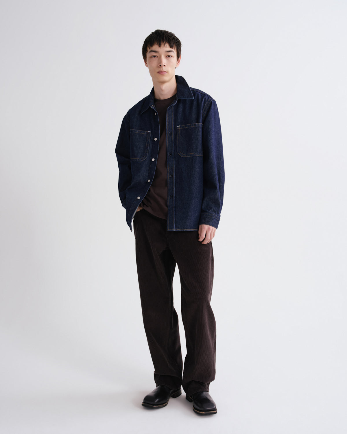 Person wearing a dark denim jacket and black pants on a white background