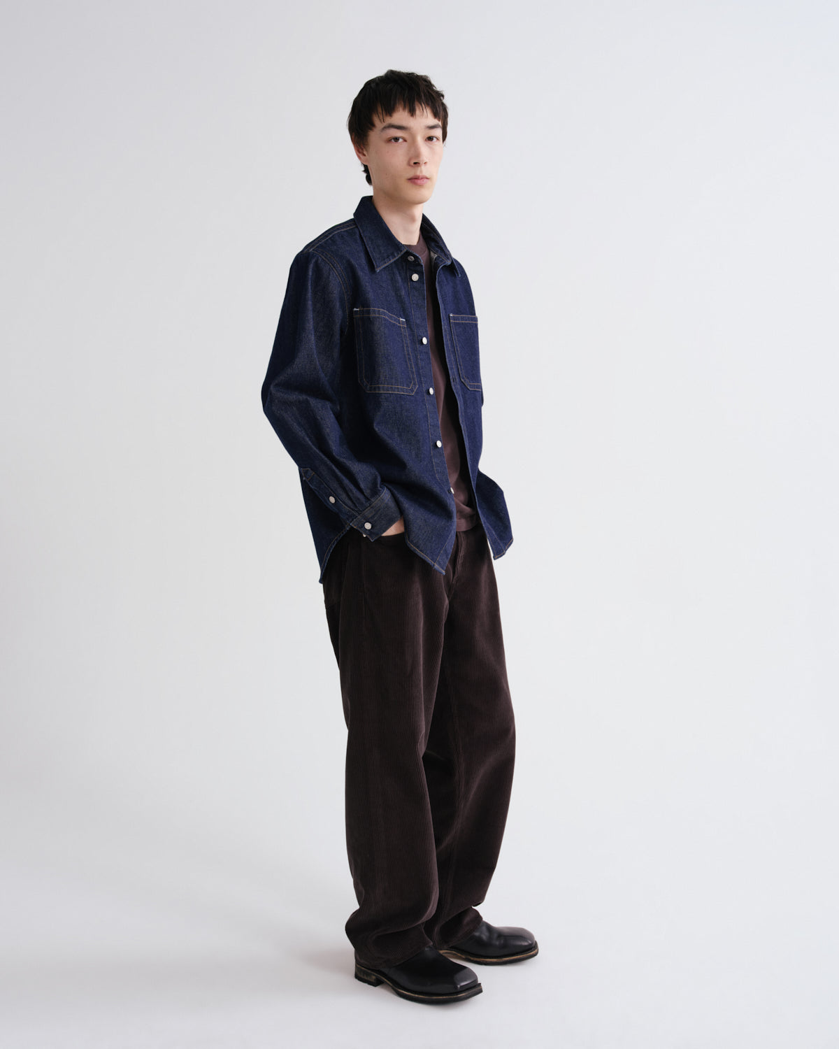 Person wearing a dark denim jacket and brown pants on a white background