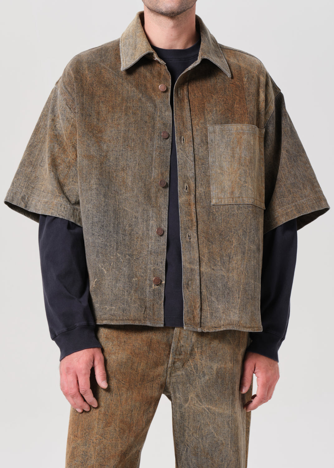 Person wearing a brown button-up shirt over a black shirt with a plain background