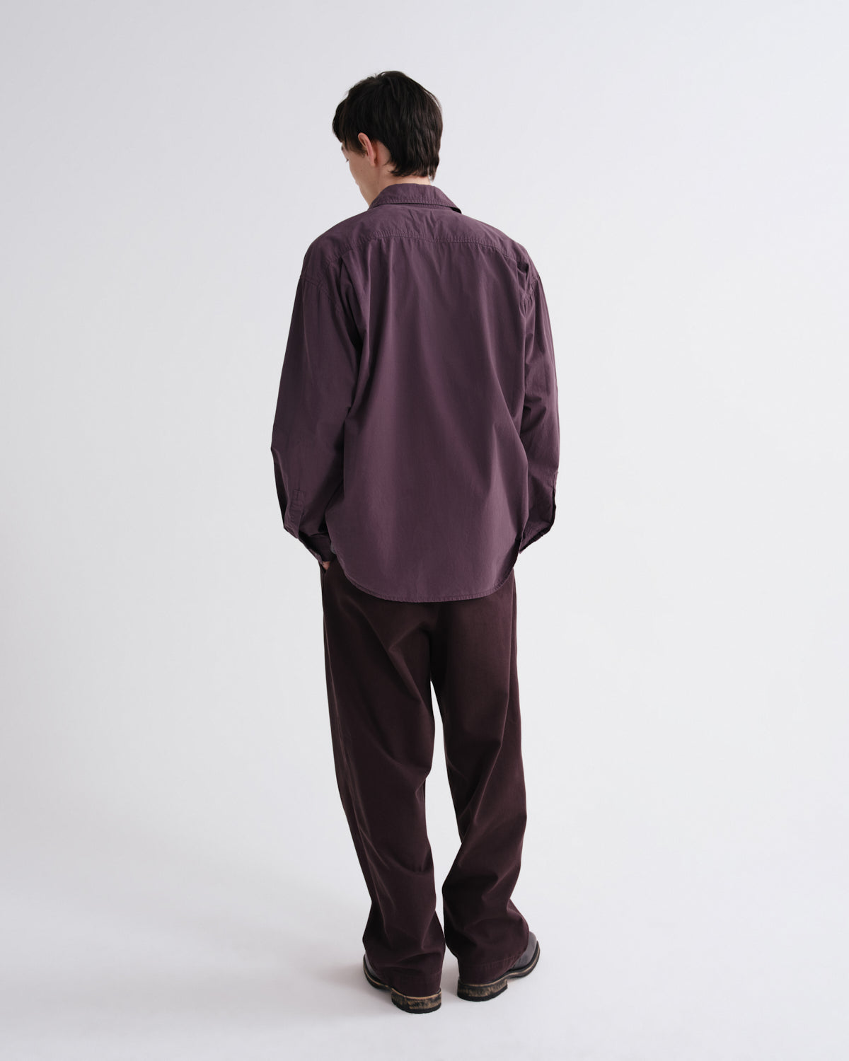 Person wearing a dark purple shirt and pants on a white background