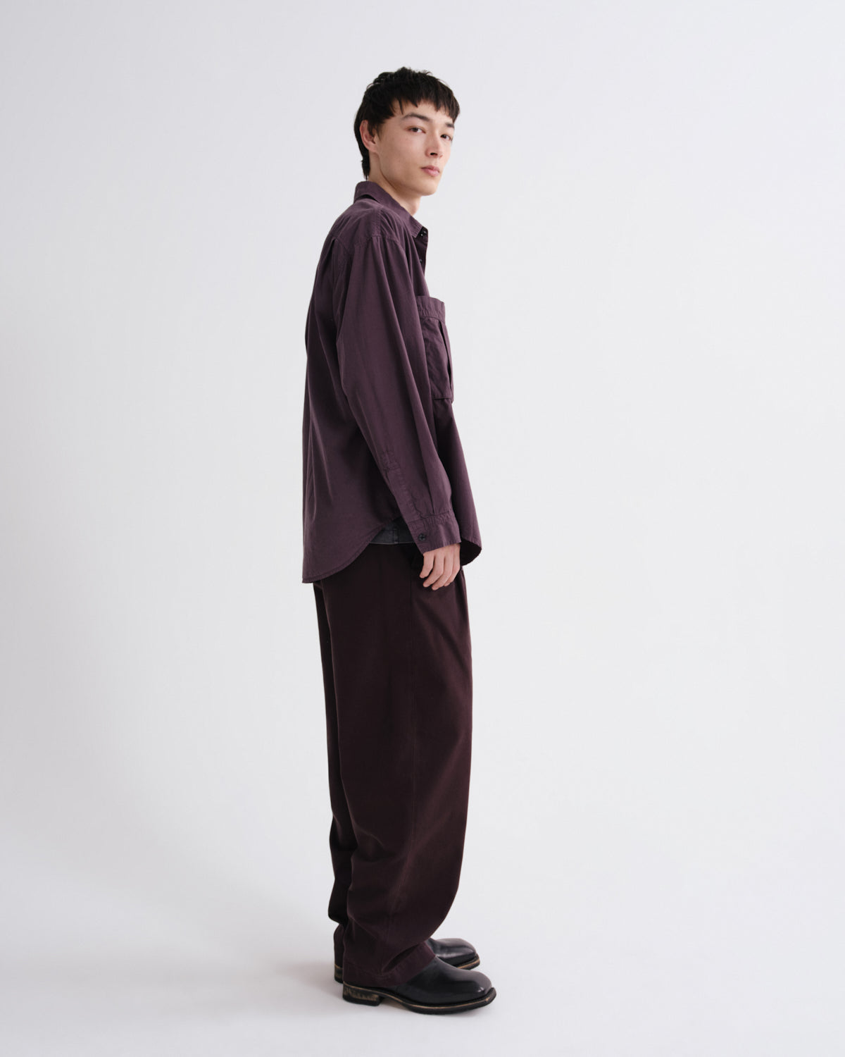 Person wearing a dark purple shirt and pants on a white background