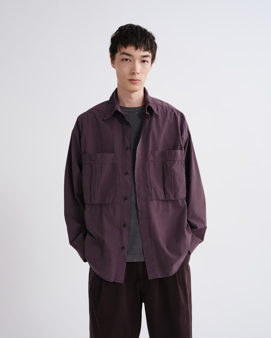 Person wearing a dark purple jacket over a gray shirt on a white background