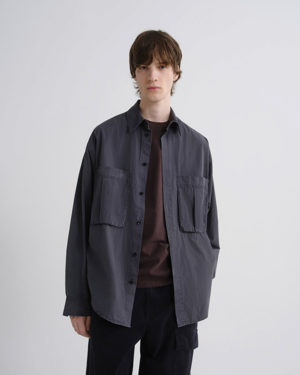 Man wearing a dark gray jacket over a brown shirt on a white background