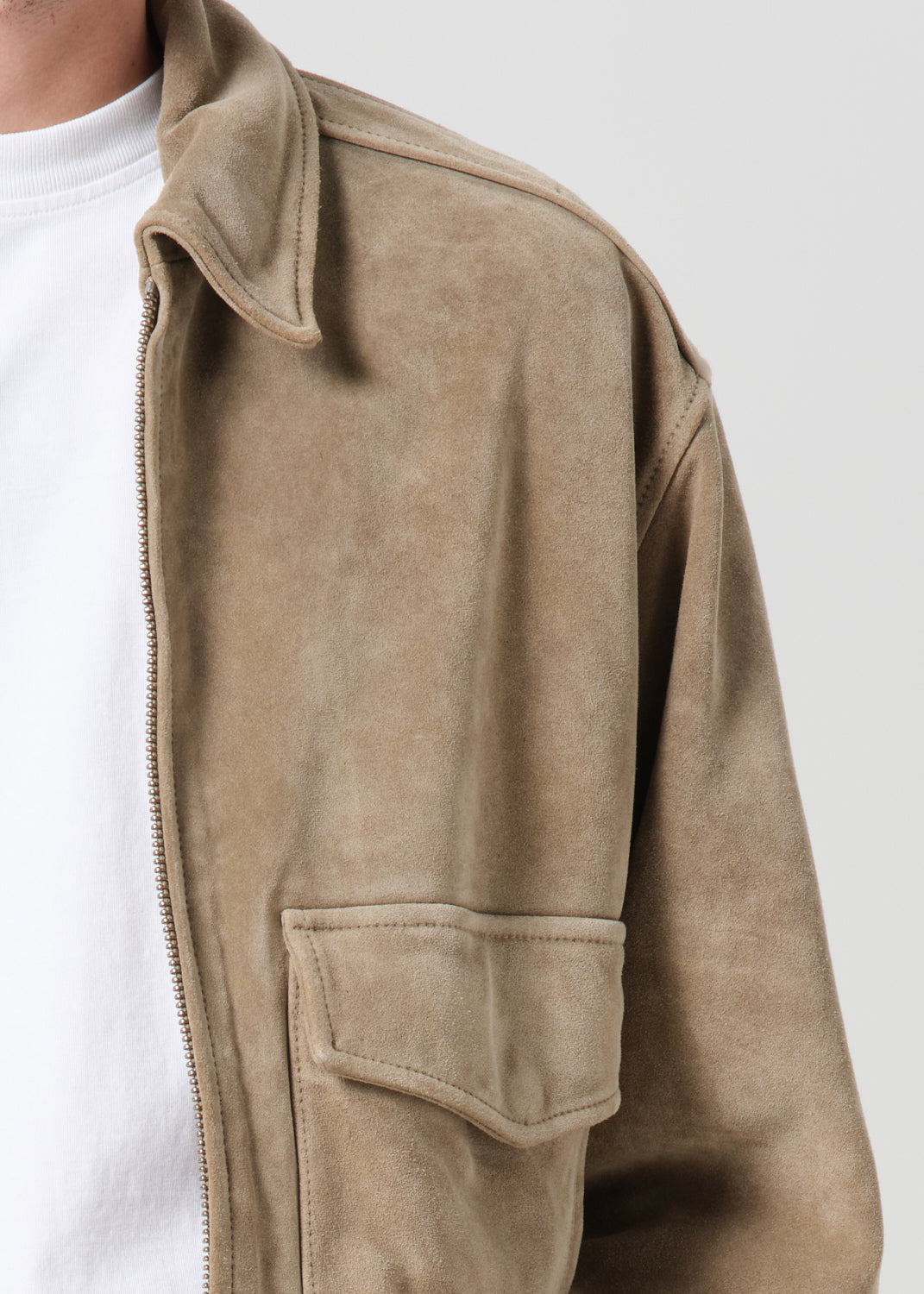 Close-up of a beige jacket with a white shirt underneath on a plain background