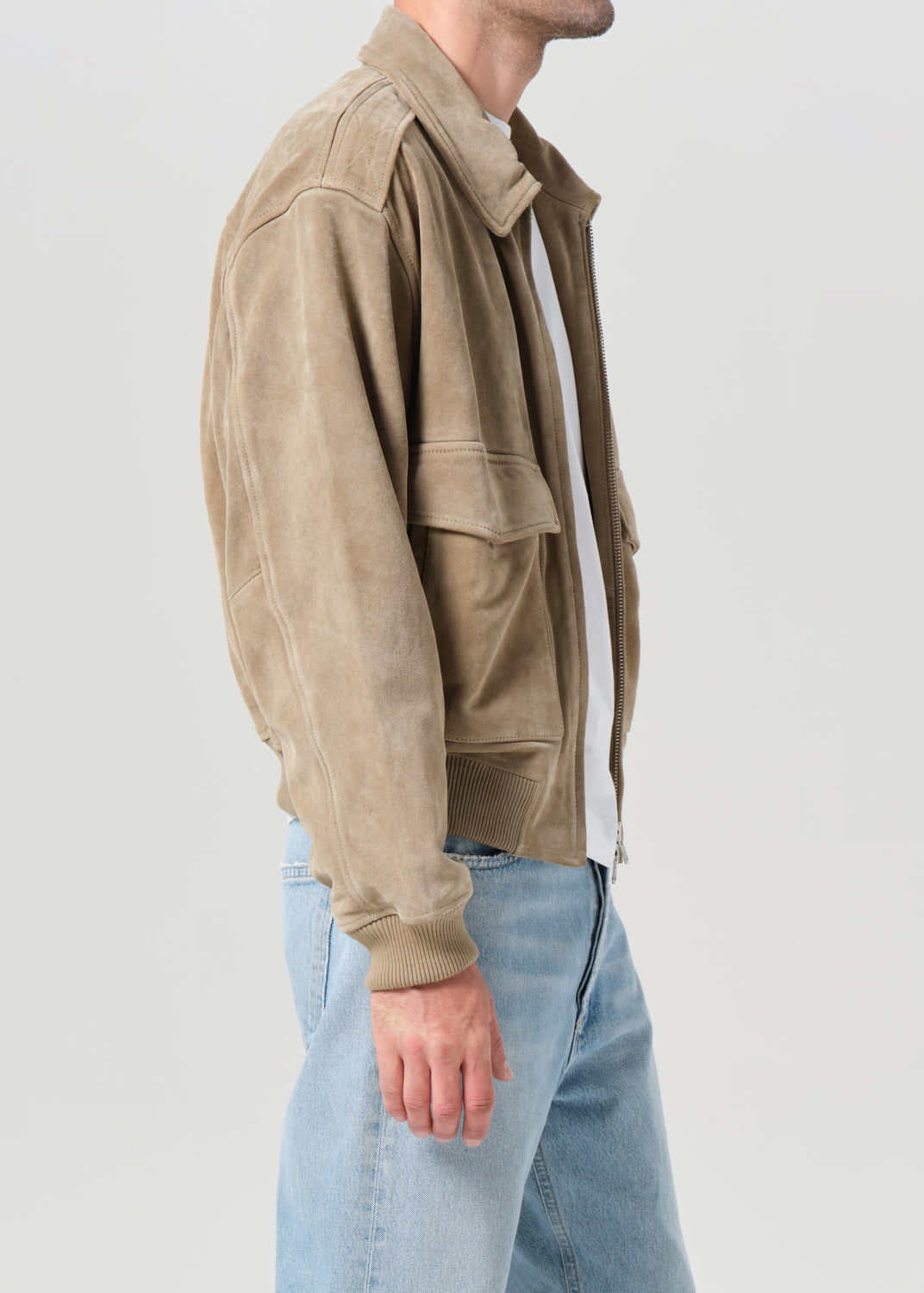 Person wearing a beige suede jacket and light blue jeans on a plain background