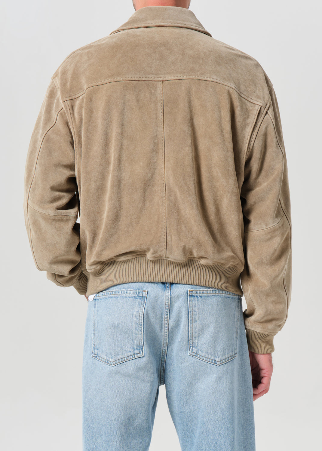Person wearing a beige suede jacket and light blue jeans on a plain background