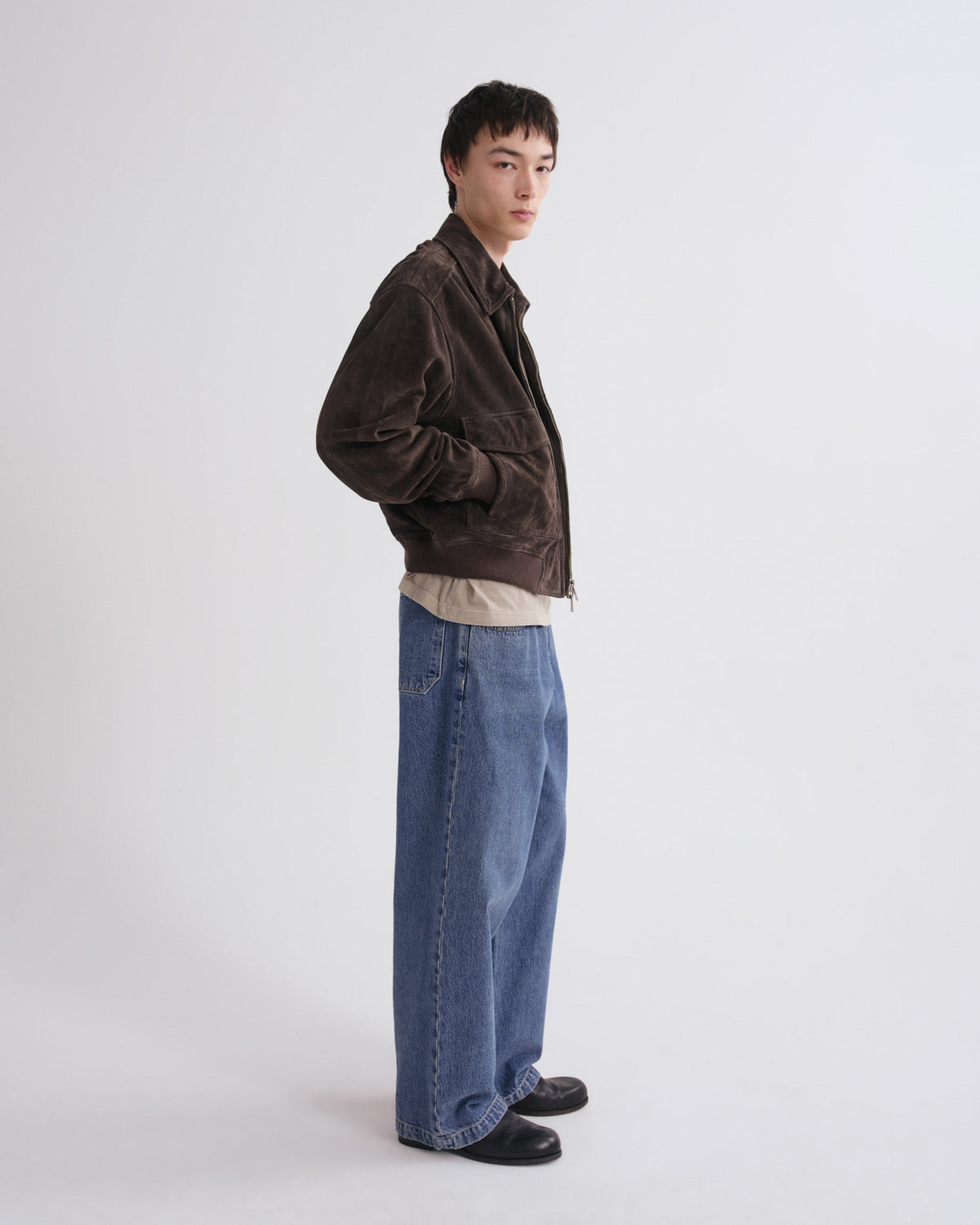 Person wearing a brown jacket and blue jeans on a white background