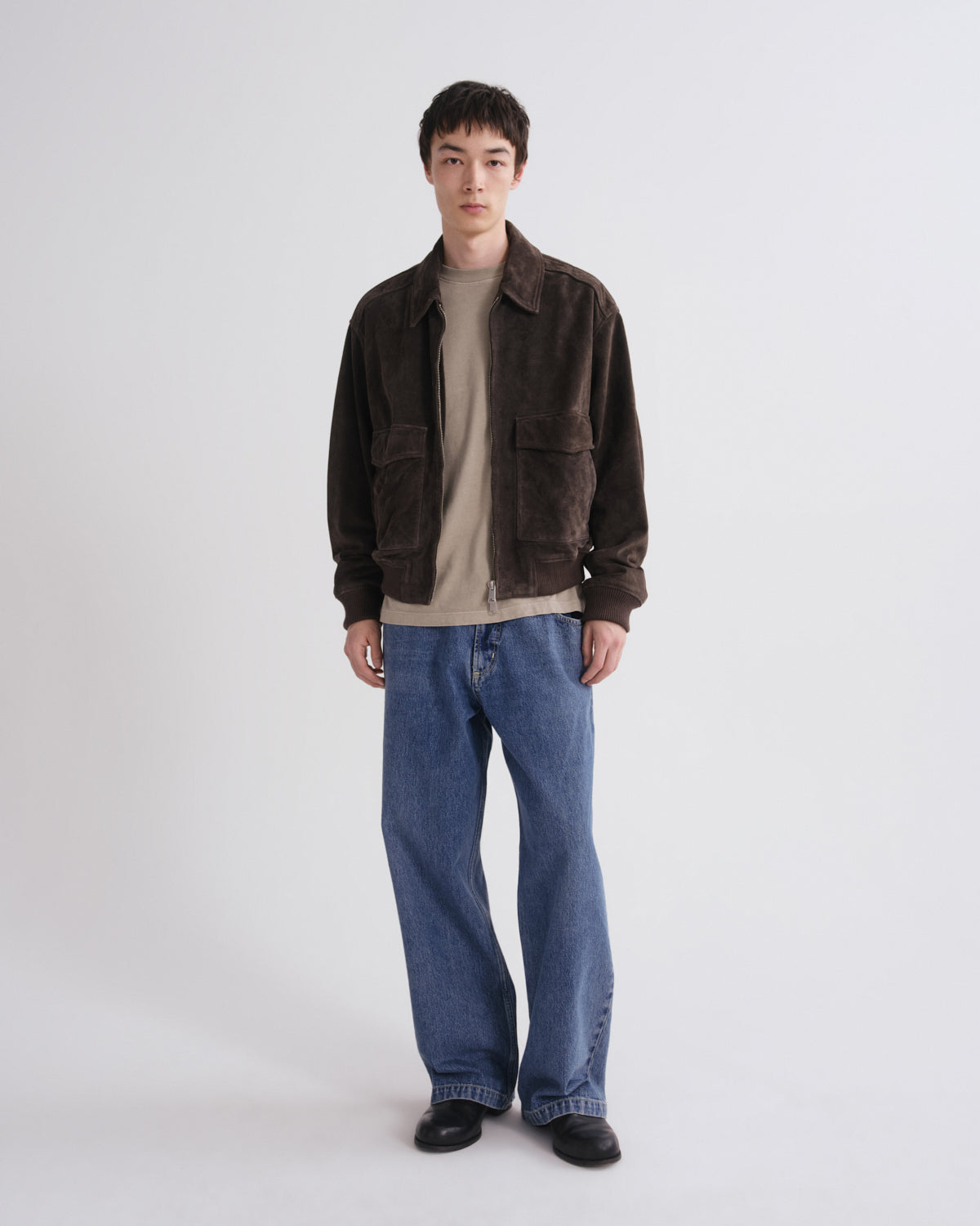 Person wearing a brown jacket, beige shirt, and blue jeans on a white background