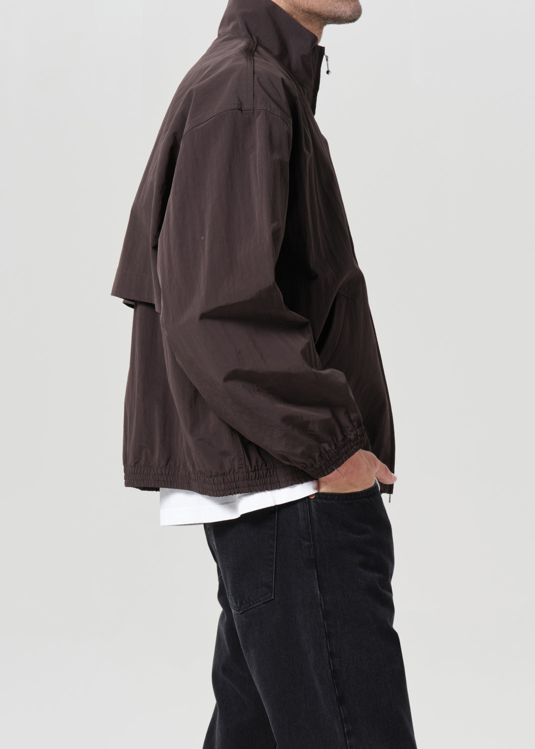 Person wearing a brown jacket and black pants on a plain background