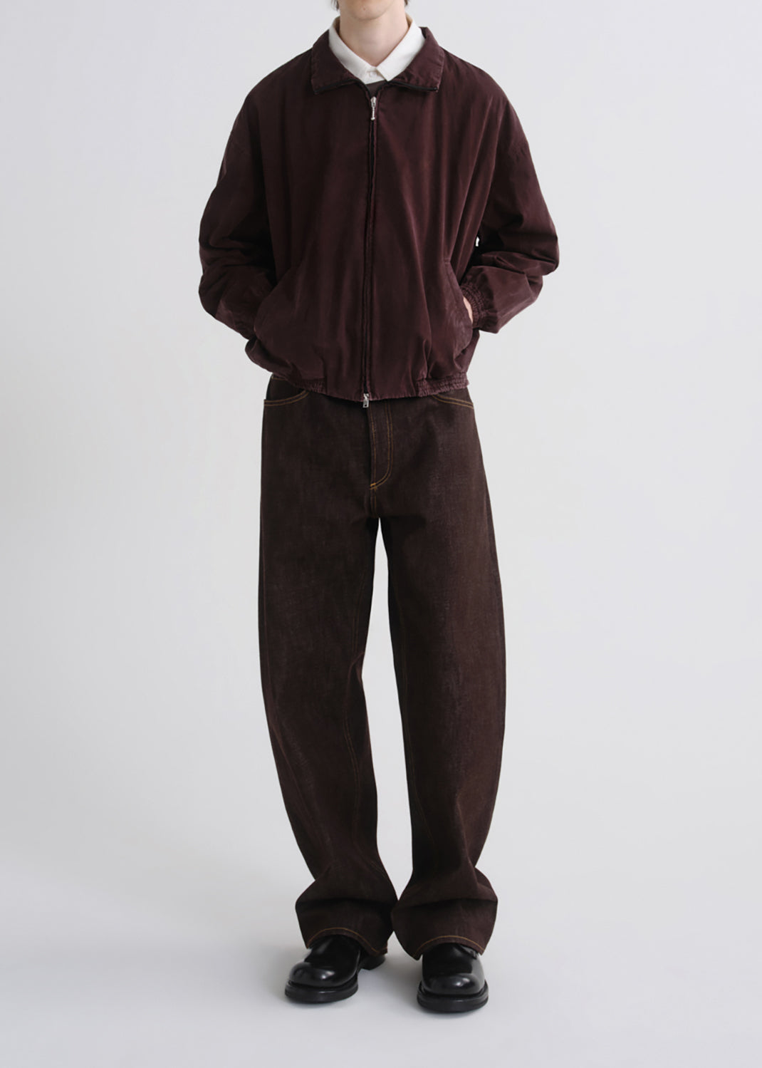 A model wearing a dark brown corduroy zip-up jacket over a white collared shirt, paired with matching dark brown corduroy trousers and black leather shoes, against a grey background.
