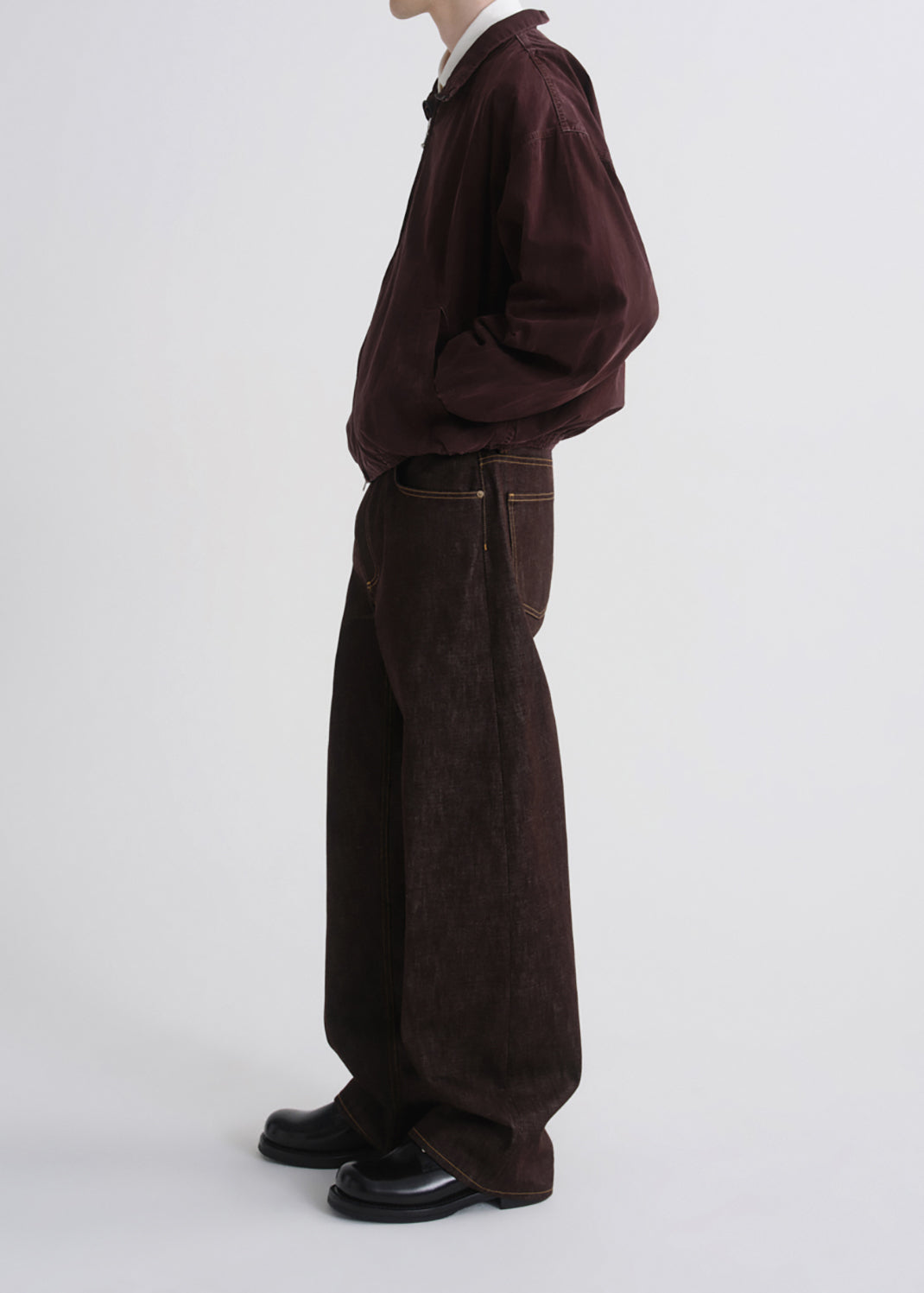 A model shown from the side wearing a dark brown corduroy jacket, matching wide-leg corduroy trousers, a white collared shirt, and black leather shoes against a grey background.