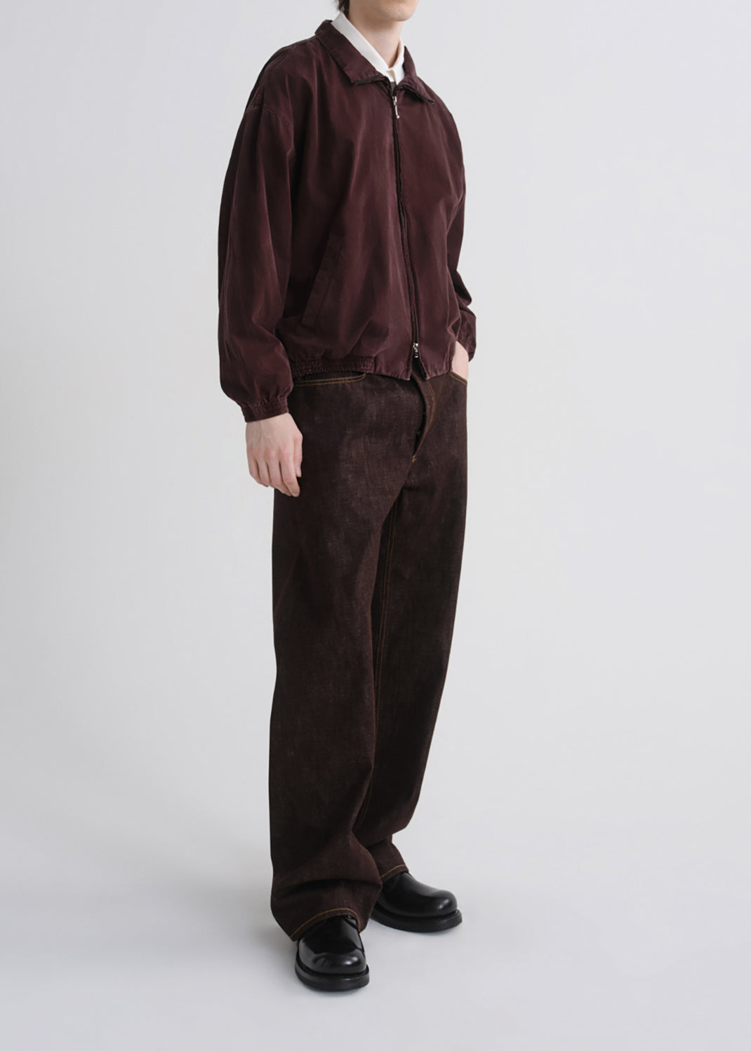 A model wearing a dark burgundy zip-up jacket and matching dark brown corduroy trousers, paired with black leather shoes, against a grey background.