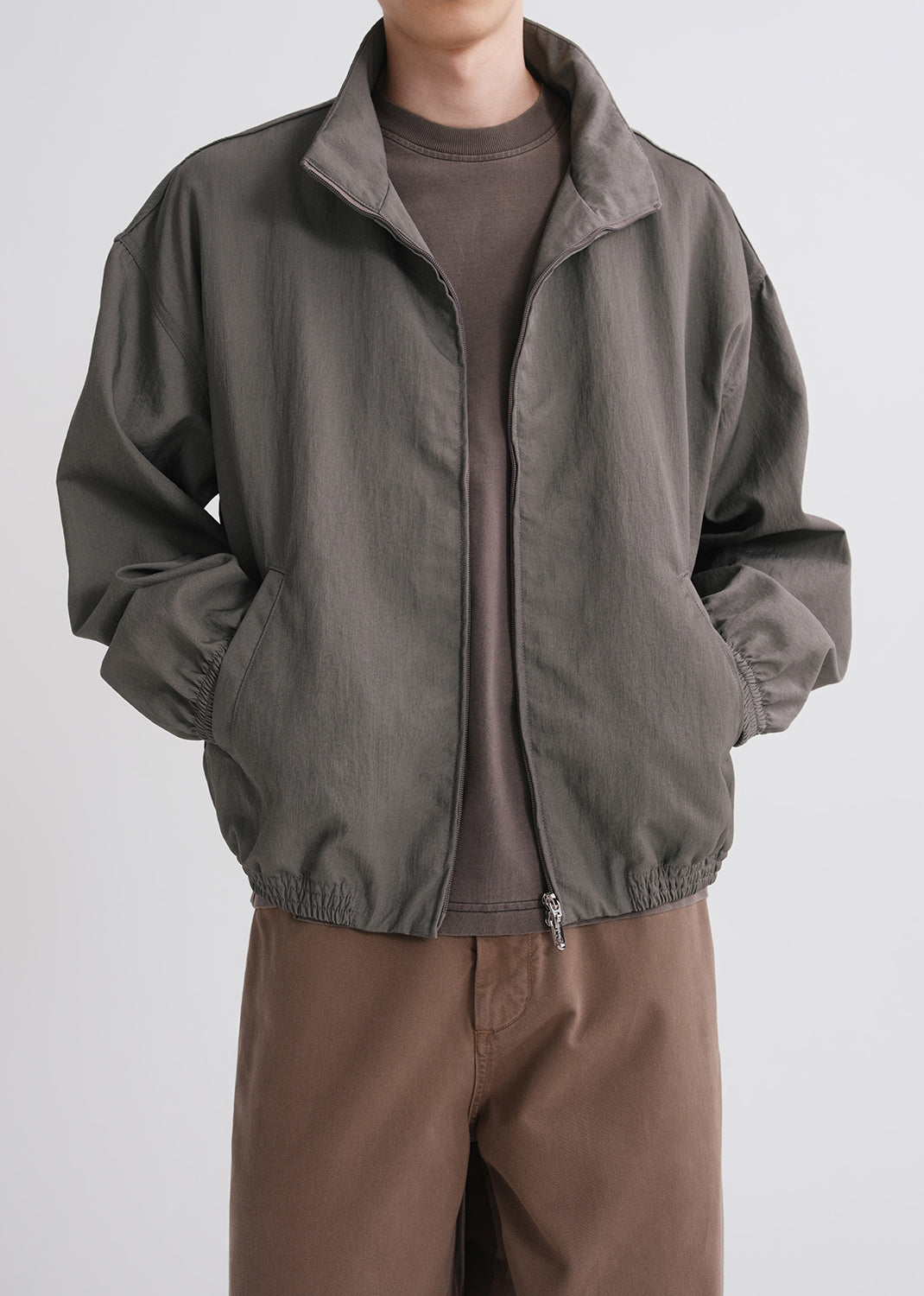 Person wearing green jacket over brown shirt and brown pants on a grey background