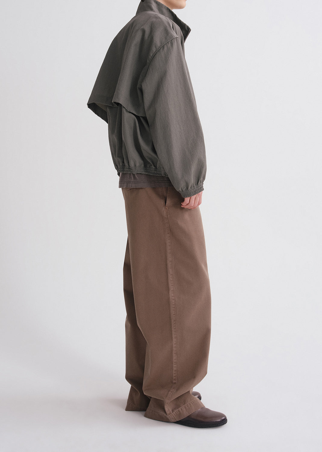 Person wearing a brown jacket and pants on a grey background