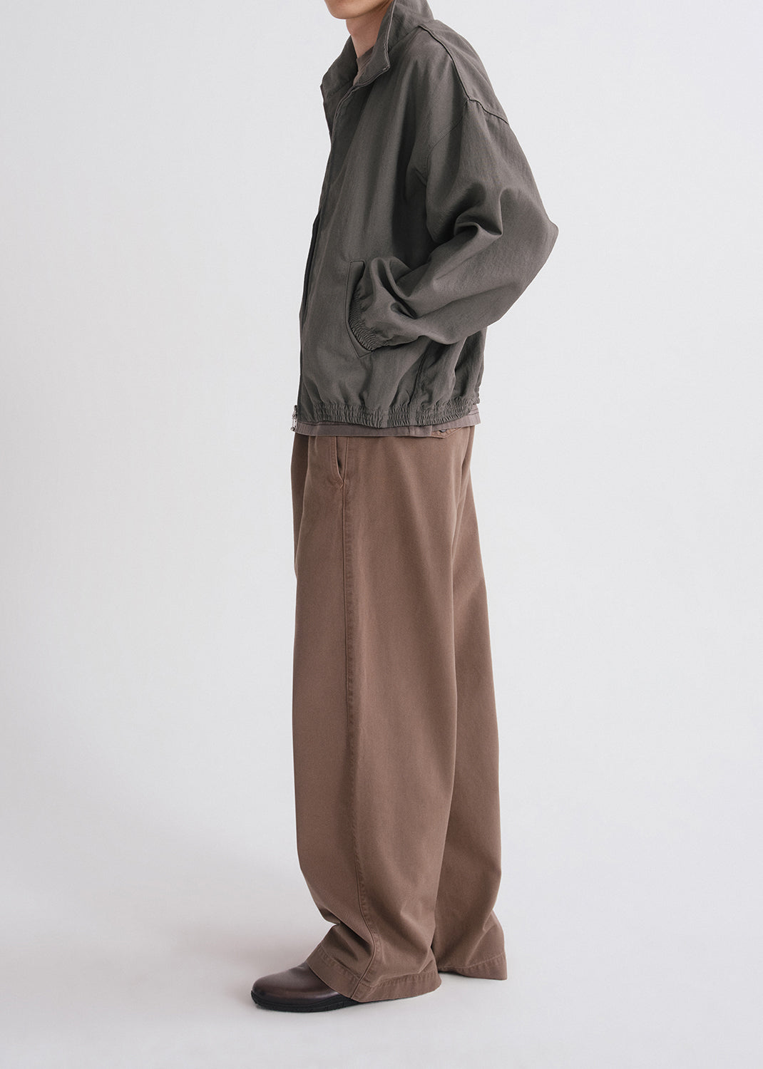 Person wearing a green jacket and brown pants on a grey background